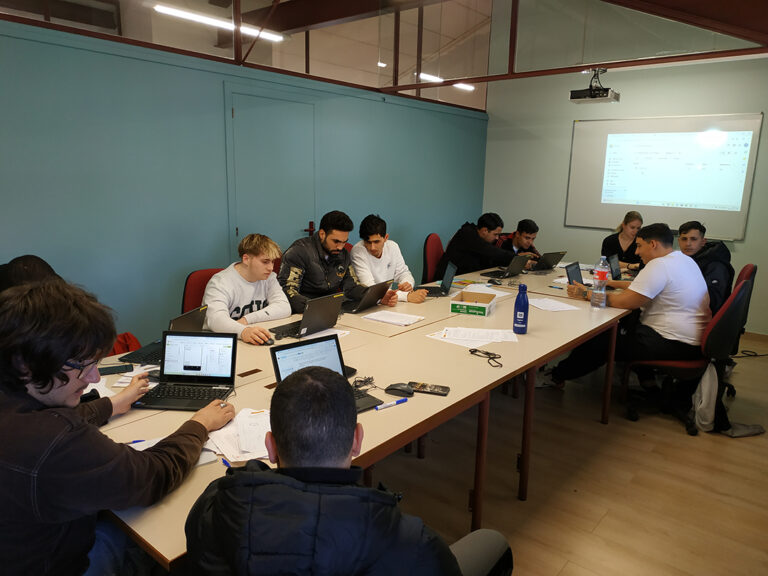 Grup de joves al voltant d'una taula, treballant conjuntament amb ordinadors portàtils.